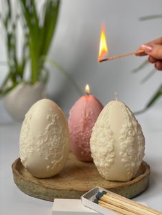 someone lighting candles in the shape of eggs on a wooden tray next to some matches