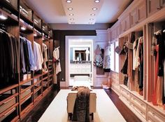 a walk - in closet with lots of clothes hanging on the walls and drawers, along with a bench