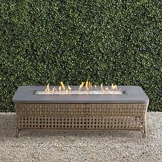 a fire pit sitting on top of a gravel ground next to a green hedge wall