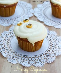 three cupcakes with white frosting and smiley faces on them sitting on doily