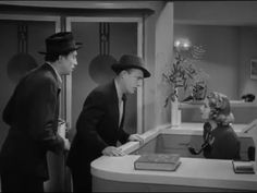 two men and a woman standing in front of a counter with a book on it