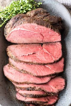 sliced roast beef in a bowl with herbs on the side, ready to be cooked