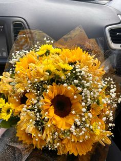 a bouquet of sunflowers sits in the front seat of a car, with baby's breath