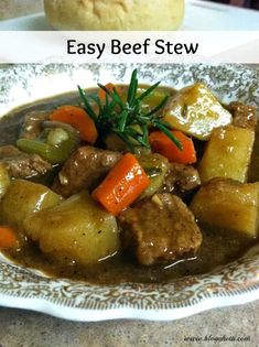 beef stew with carrots and potatoes in a white bowl on a table next to a roll