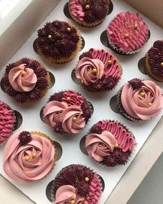 twelve cupcakes with pink frosting and purple icing in a white box