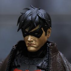 a close up of a batman action figure wearing a black mask and red cape with spikes on his head