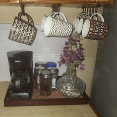 coffee mugs are hanging on the wall above a shelf with jars and cups in it