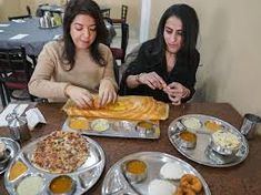 two women sitting at a table with plates and trays of food in front of them