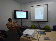 a man is giving a presentation in front of a projector screen with a projector on it