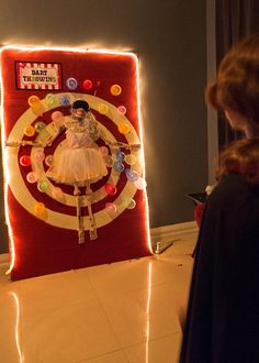 a woman standing in front of a display with buttons and lights on the wall behind her