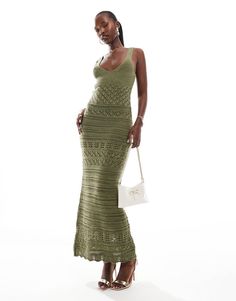 a woman in a green crochet dress holding a white purse and posing for the camera