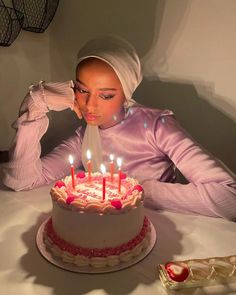 a woman blowing out candles on a cake with pink frosting and white icing