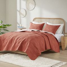 a bed with an orange comforter and pillows in a room next to a plant