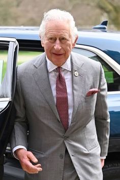 an older man in a suit and tie standing next to a car