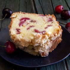 a piece of cake sitting on top of a black plate next to cherries and a fork