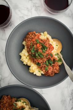 two bowls filled with mashed potatoes, meat sauce and garnished with parsley