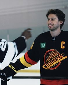 a man in black jersey standing next to an ice hockey goalie with his arms out