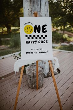 a sign sitting on top of a wooden easel in front of a tree trunk