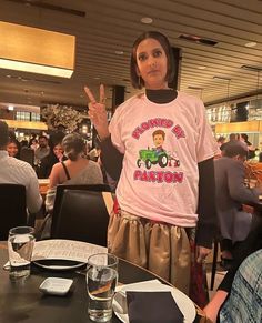 a woman standing in front of a table at a restaurant wearing a pink shirt with an image of a farmer on it