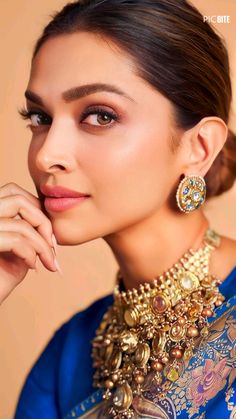 a woman in a blue dress with gold jewelry on her neck and hand near her face