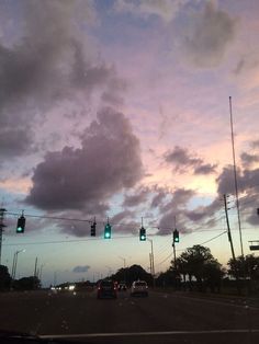 traffic lights are green as the sun sets in the sky over an intersection with cars