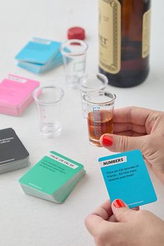 a person holding up a business card next to several different colored cards and liquor bottles