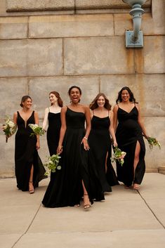 a group of women standing next to each other wearing black dresses and holding bouquets