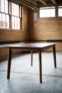 a wooden table sitting in an empty room with brick walls and windows on either side