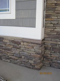 the corner of a house with some rocks on it and a window in the background