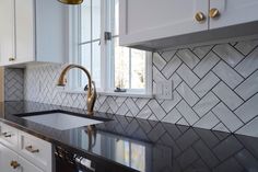 a kitchen with white cabinets and black counter tops, gold faucet, marble backsplash