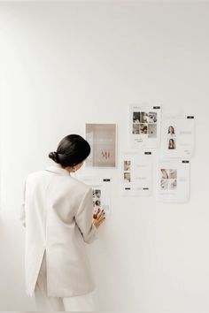 a woman standing in front of a white wall with pictures on the wall and posters behind her