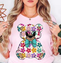 Colorful Daisy Teddy Bear (Tee) | Spring Fashion | Unisex Pre-Shrunk T-Shirt   Embrace the spirit of spring with our vibrant color palette, featuring pastel hues and refreshing tones that capture the essence of nature's awakening. Whether you're strolling through blooming gardens or enjoying a picnic in the park, our adorable and chic spring t-shirts will effortlessly elevate your spring wardrobe.   Key Features: High-Quality Material: Made from the softest washed, garment-dyed, and durable fabr Colorful Short Sleeve T-shirt For Spring, Cute Multicolor T-shirt For Spring, Multicolor Tops With Funny Print For Spring, Casual Multicolor Print T-shirt For Spring, Multicolor Print Short Sleeve T-shirt For Spring, Multicolor Cartoon Print T-shirt For Spring, Multicolor Summer T-shirt With Front Print, Playful Colorful Crew Neck T-shirt, Spring Multicolor Graphic Print T-shirt