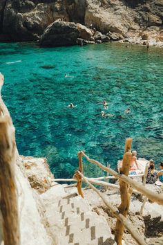 people are swimming in the blue water near some rocks and stairs that lead down to the beach