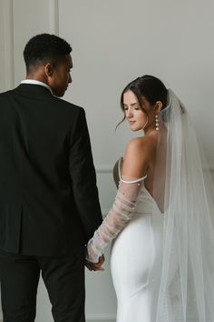 the bride and groom are looking at each other in their wedding attire, holding hands