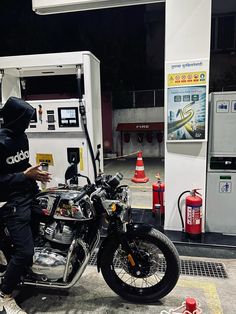 a man sitting on a motorcycle in front of a gas station with an open fuel pump