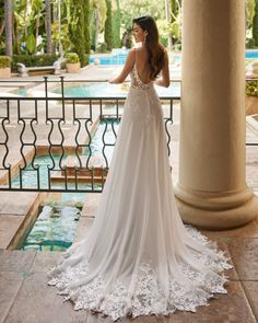 a woman standing in front of a pool wearing a wedding dress with an open back