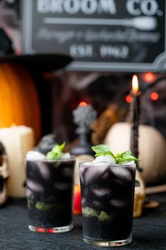 two halloween cocktails sitting next to each other on a table with candles and decorations