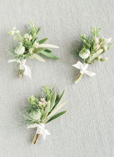 three boutonnieres with white flowers and greenery on the top one is green