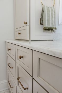 a bathroom with white cabinets and marble counter tops, gold pulls on the handles in front of the mirror