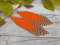 an orange and yellow beaded brooch sits on a wooden table next to leaves