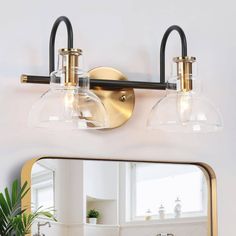 a bathroom vanity light with two clear glass shades on it's sides and a mirror above the sink