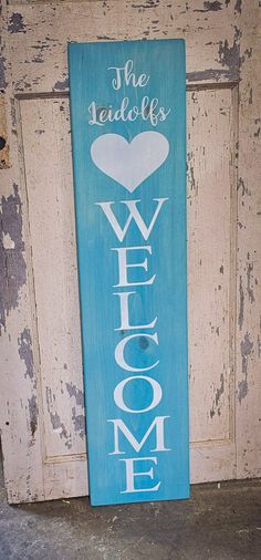 a blue welcome sign sitting on the side of a door with a heart in it