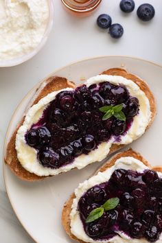 two pieces of bread with blueberries and cream on them sitting on a white plate