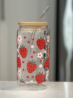 a glass jar with strawberries and flowers painted on the lid is sitting on a counter