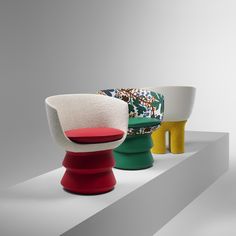 three different colored chairs sitting on top of a white shelf with one red chair in the middle