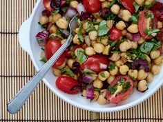 a white bowl filled with chickpeas, tomatoes and spinach on top of a bamboo mat