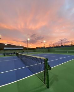 a tennis court with the sun setting in the background and lights shining on the courts