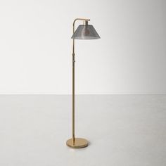 a brass floor lamp with a grey shade on the top and a white wall in the background