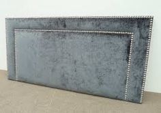 a gray headboard with silver studded trim on top and bottom, against a white wall