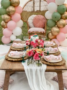 a table set up for a party with pink and green balloons, plates and napkins